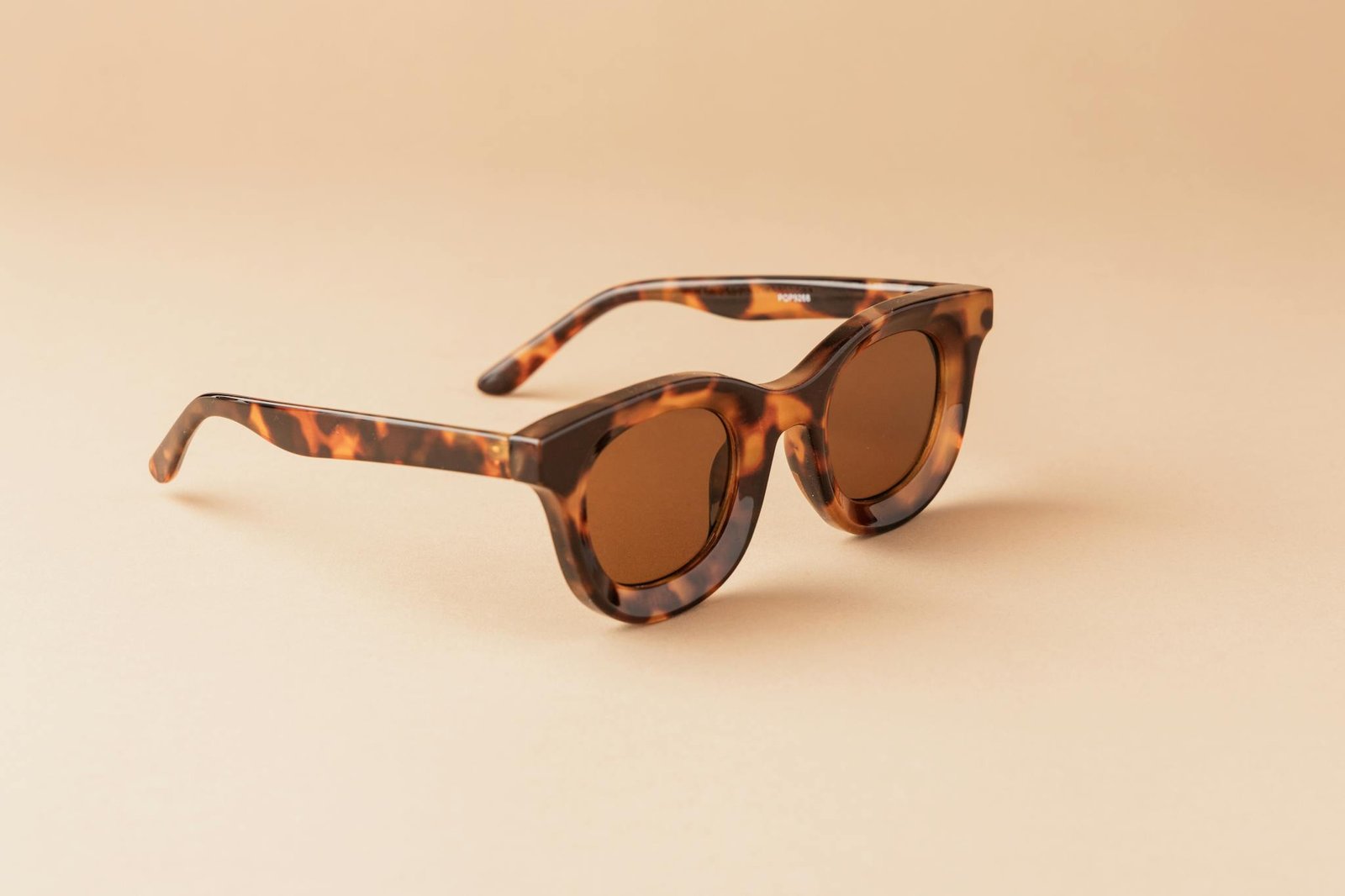 Elegant tortoiseshell sunglasses with brown lenses creatively displayed on a simple beige backdrop.