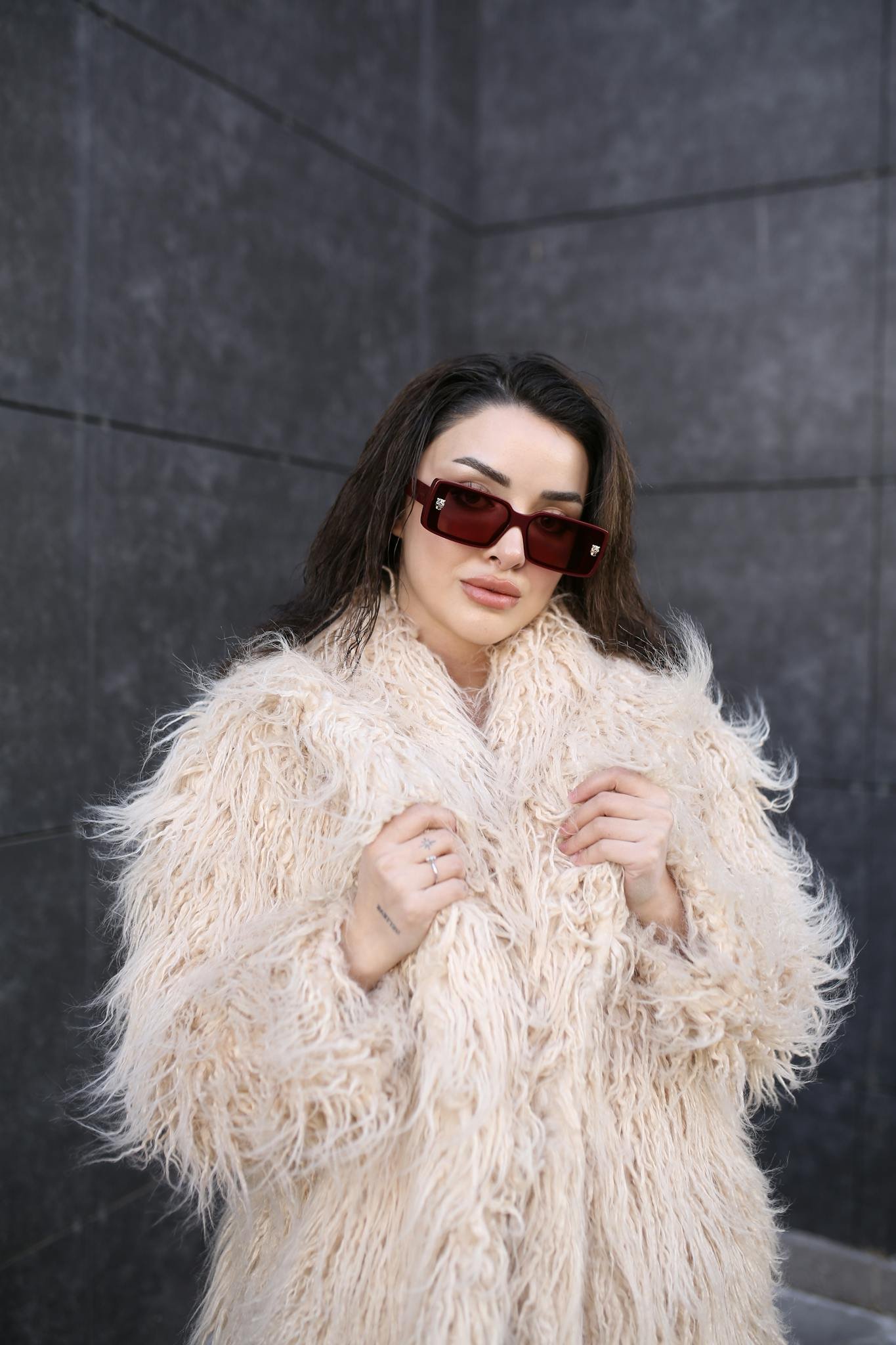 Elegant woman posing outdoors in a fur coat and sunglasses, showcasing fashionable style.