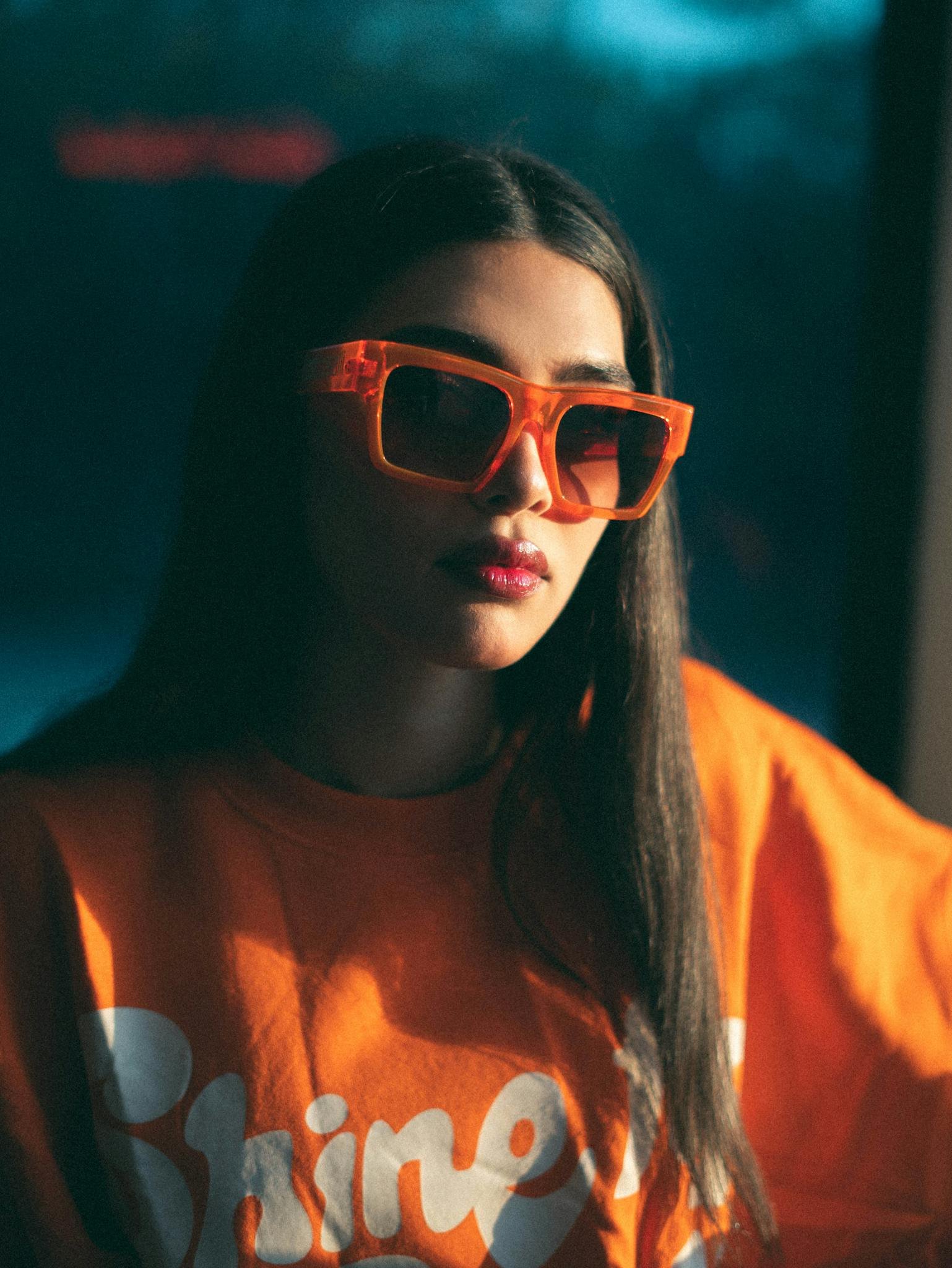 Fashionable woman wearing oversized orange sunglasses and shirt, exuding a trendy, vibrant style.