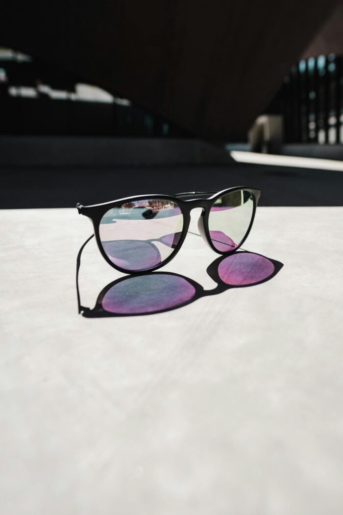 Modern sunglasses casting a shadow with colorful reflections in an urban setting.