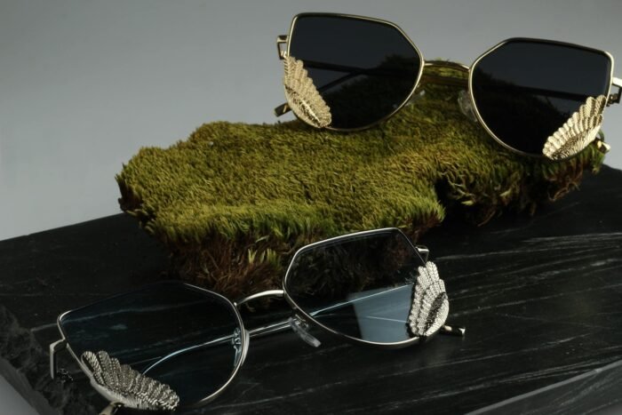 Stylish gold and silver sunglasses resting on a green moss background.