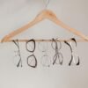 Various eyeglasses frames neatly hanging on a wooden clothes hanger with neutral background.
